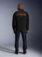 Alpinestars Revved WR Jas, zwart, achteraanzicht met groot rood 'ALPINESTARS' borduurwerk met 3D-effect, urban coachjack-stijl jas, gedragen met donkere denim jeans en zwarte sneakers, minimalistische motorkleding