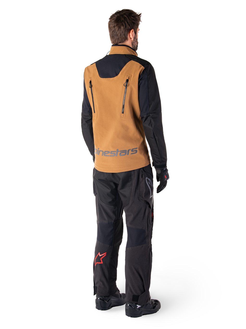 Alpinestars Hyde XT Stretch Drystar®XF Jacke und Hyde XT Drystar® Hose, Rückansicht eines Fahrers in brauner und schwarzer Adventure-Touring-Ausrüstung, Jacke mit vertikalen Reißverschlüssen am Rücken und Alpinestars-Logo, schwarze Hose mit rotem Stern-Logo an der Wade, kombiniert mit schwarzen Handschuhen und Stiefeln.