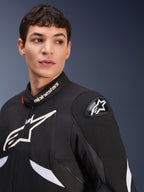 Veste Alpinestars T-GP R V3 Drystar®, noir et blanc, portée par un mannequin homme, avec des logos Alpinestars blancs sur le col et la poitrine, slider d'épaule DFS noir avec une étoile blanche, photo lifestyle détaillée d'une veste textile de sport imperméable