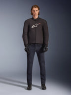 Model trägt die wasserdichte Alpinestars SMX Jacke in Schwarz mit weißem und rotem Logo, kombiniert mit einer dunklen Denim-Motorradhose, schwarzen Handschuhen und Motorradstiefeln, sportliches Allwetter-Motorrad-Outfit