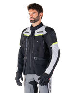 Alpinestars Bogotá Pro Drystar® Jacket, adventure touring motorcycle jacket, Black Ice Gray and Yellow Fluo, worn by a man with matching gray pants and black gloves, featuring technical ventilation panels and multi-pocket design.