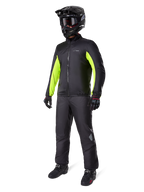 Motorcyclist wearing Alpinestars Bogotá Pro Drystar® Jacket liner, Black with bright Yellow Fluo panels on the sleeves, worn with matching black pants, black motocross helmet, and gloves, waterproof all-season adventure gear
