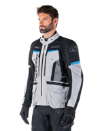 Alpinestars Bogota' Pro Drystar® Jacke, Eisgrau, Schwarz und Cyan, Adventure-Motorradjacke getragen von einem Mann mit schwarzen Handschuhen, technisches Design mit mehreren Taschen und Belüftungspanelen, Hochleistungs-Fahrerausrüstung