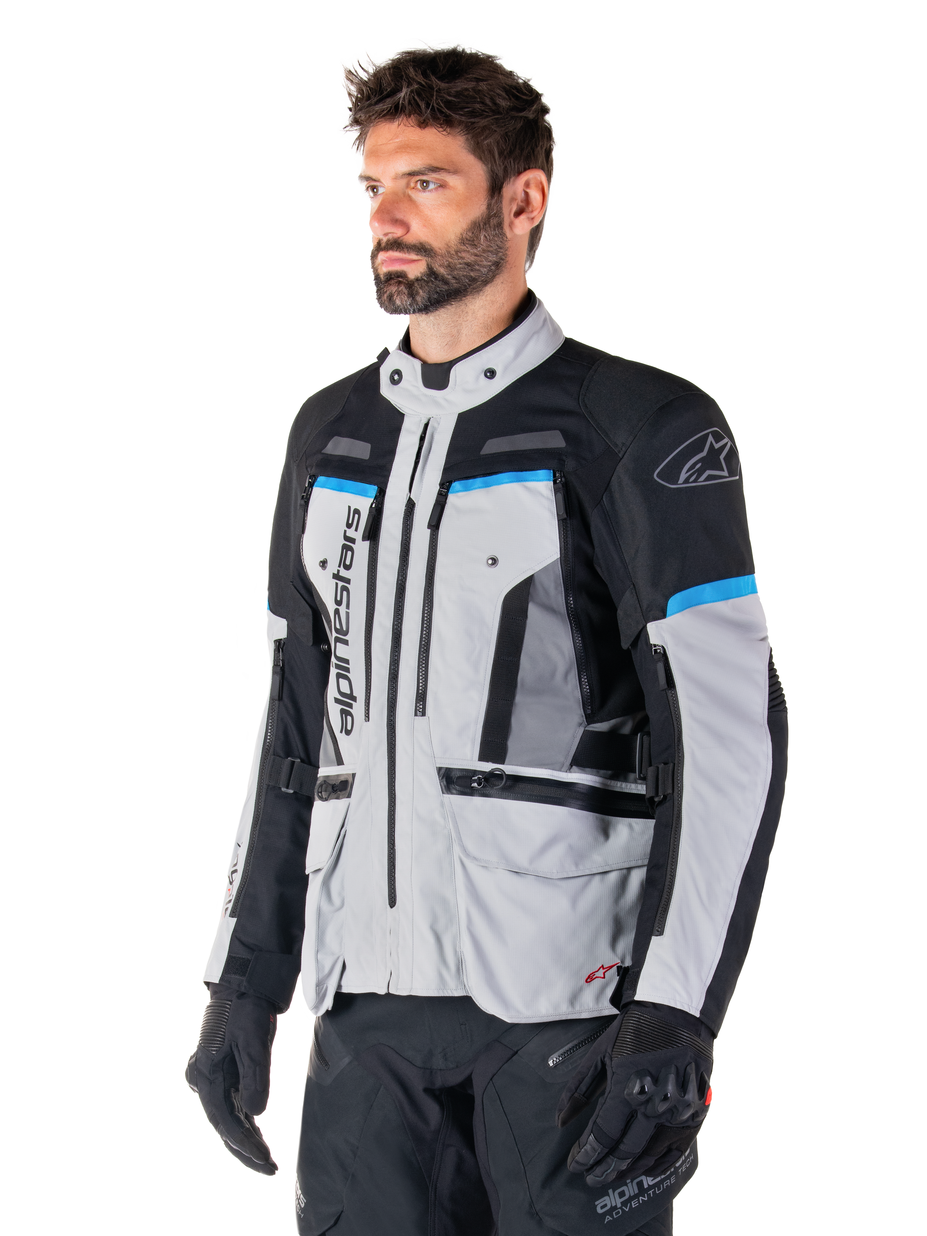 Alpinestars Bogota' Pro Drystar® Jacke, Eisgrau, Schwarz und Cyan, Adventure-Motorradjacke getragen von einem Mann mit schwarzen Handschuhen, technisches Design mit mehreren Taschen und Belüftungspanelen, Hochleistungs-Fahrerausrüstung