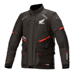 Honda Andes V3 Drystar motorjas, motor touringjas, zwart met rode accenten, vooraanzicht met grote cargozakken en verstelbare riemen, technische textielconstructie met Honda-vleugel en Alpinestars-logo's, adventure-geïnspireerd ontwerp
