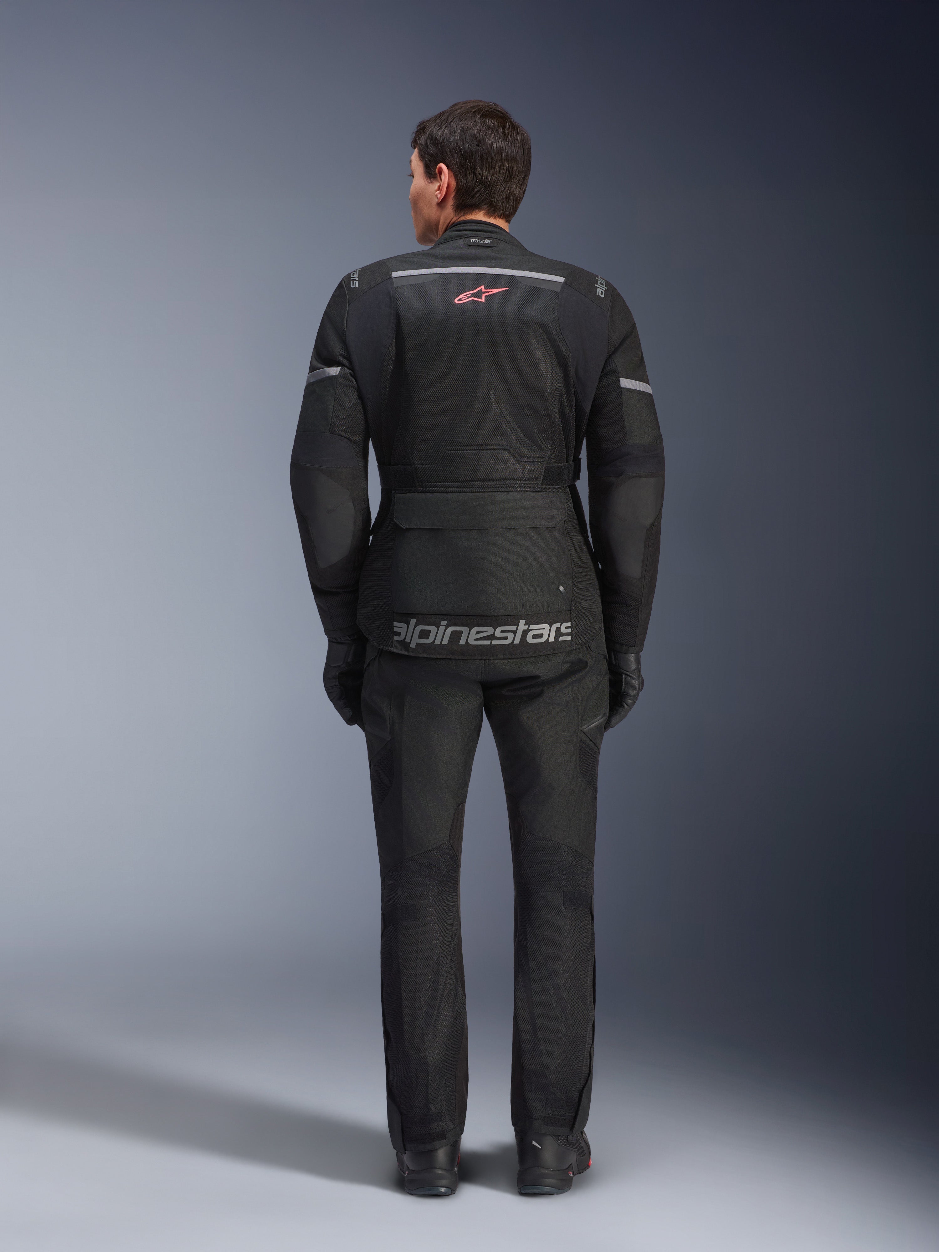 Alpinestars Andes Air Drystar® jas en broek, zwarte motor touringoutfit, achteraanzicht van de rijder, voorzien van mesh-panelen, rood sterlogo en reflecterende Alpinestars-branding op de jas, gedragen met zwarte handschoenen en laarzen.