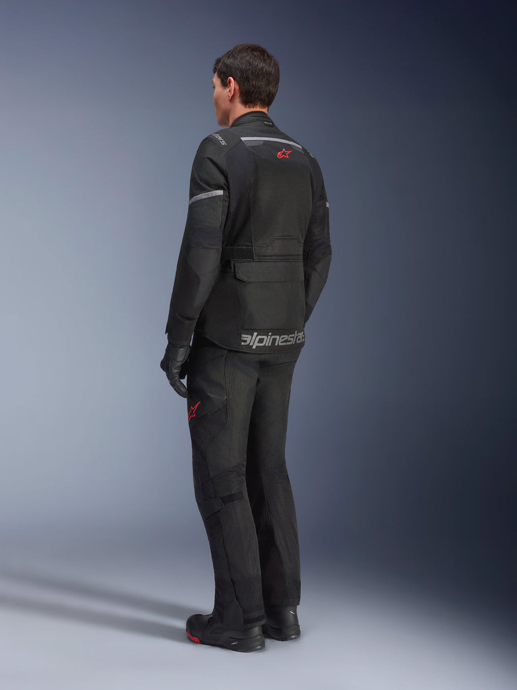 Alpinestars Andes Air Drystar® Jas, zwart, achteraanzicht op een motorrijder, met uitgebreide mesh-panelen voor ventilatie, gedragen met bijpassende adventure motorbroek en laarzen, toont het weggeoriënteerde touring-ontwerp en de branding.