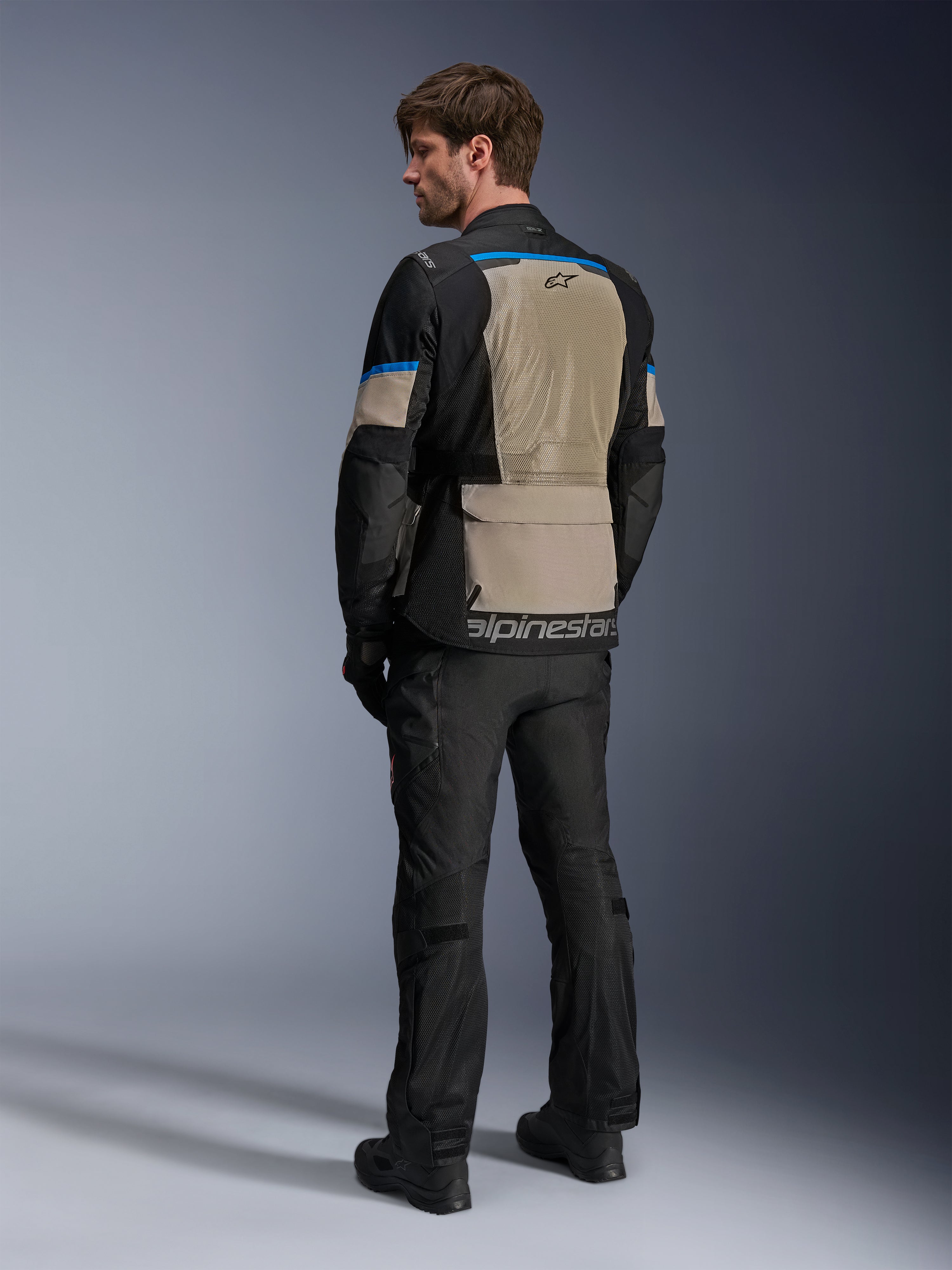 Alpinestars Andes Air Drystar® Jacke, Schwarz, Laurel Gray und Bright Blue, Rückansicht mit großem Mesh-Belüftungspanel am Rücken, Logo am unteren Saum, getragen mit schwarzer Motorradhose und Stiefeln.