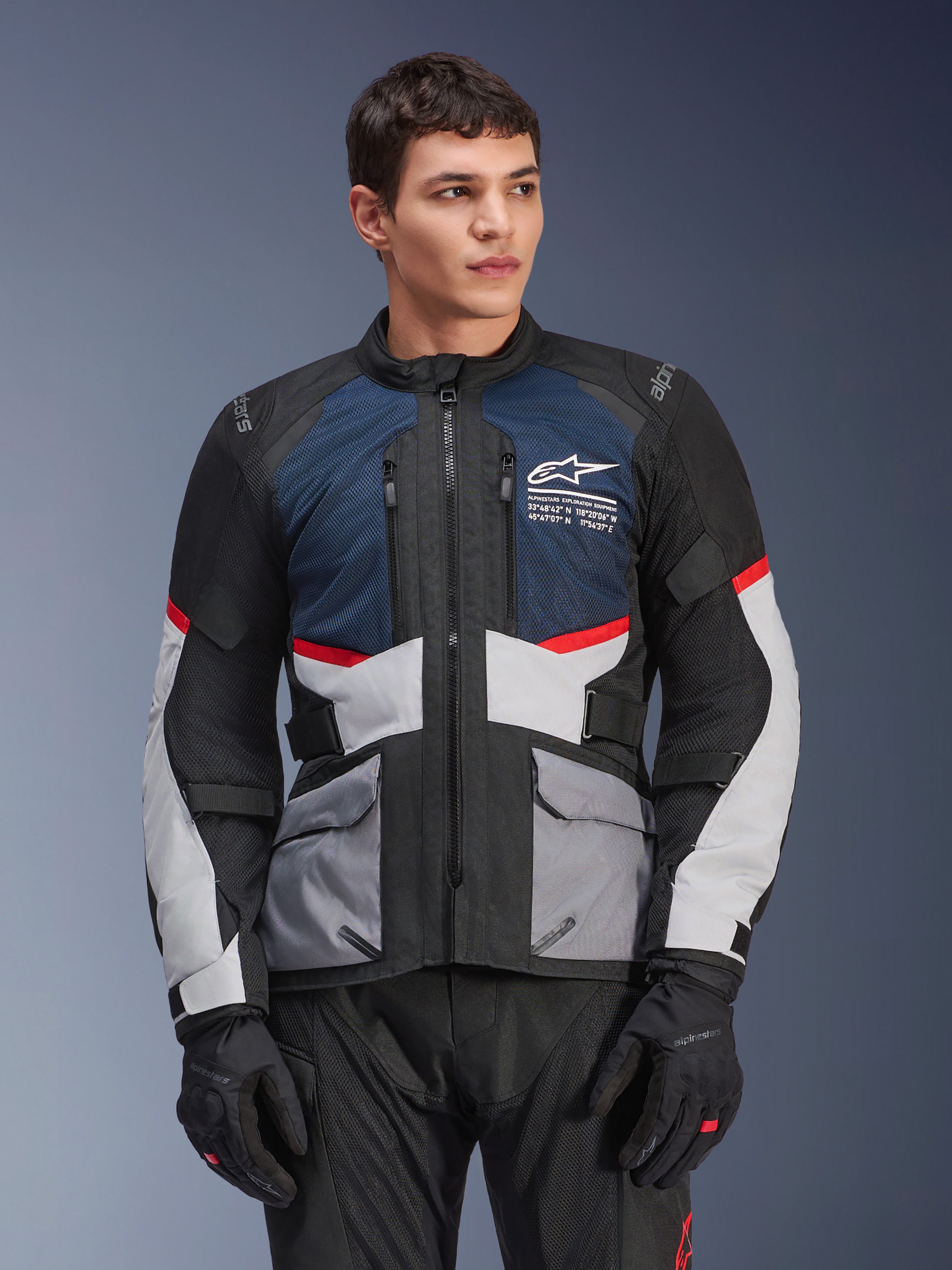 Alpinestars Andes Air Drystar motorjas, touring motorjas voor heren, diepblauw, zwart en ijsgrijs met rode accenten, gedragen door een mannelijk model met zwarte handschoenen, voorzien van mesh ventilatiepanelen en handige zakken aan de voorkant, moderne adventure en touruitrusting