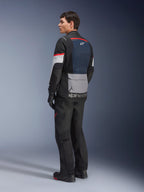 Männliches Model in der Rückansicht von der Seite, das die Alpinestars Andes Air Drystar® Jacke in Deep Blue Black Ice Gray trägt, kombiniert mit schwarzer Motorradhose und Handschuhen, mit blauem Mesh-Rückeneinsatz, grauer Utility-Tasche am unteren Rücken und roten Akzenten an den Ärmeln, professionelle Adventure-Touring-Ausrüstung.