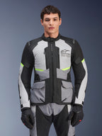 Männlicher Fahrer trägt die Alpinestars Andes Air Drystar® Jacke in Ice Gray, Dunkelgrau und Schwarz, mit neongelben Akzenten und Mesh-Belüftungseinsätzen, kombiniert mit passender Motorradhose und Handschuhen, Adventure-Touring-Ausrüstung