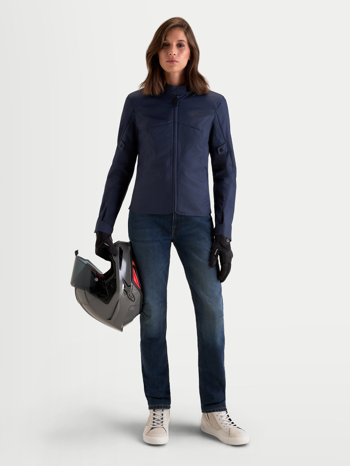 Alpinestars Stella C-1 Waterproof Jas, urbane motorjas voor dames in mood indigo blauw, gedragen door een model dat een helm vasthoudt, met duurzame polyfabric textielconstructie