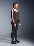 Vrouwelijk model in zijprofiel draagt de Alpinestars Stella T-Dyno WR Jas in zwart, ecru en felrood, voorzien van racestrepen op de mouwen en sterlogo's, gecombineerd met een zwarte broek en veterlaarzen voor een urban motorstijl
