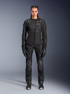 Veste Alpinestars Stella ST-2 Air, noire, vue studio en pied d'une motarde portant un pantalon et des gants de moto noirs assortis, dotée de panneaux en mesh à haute circulation d'air, de détails de logos rouges et d'un design touring moderne