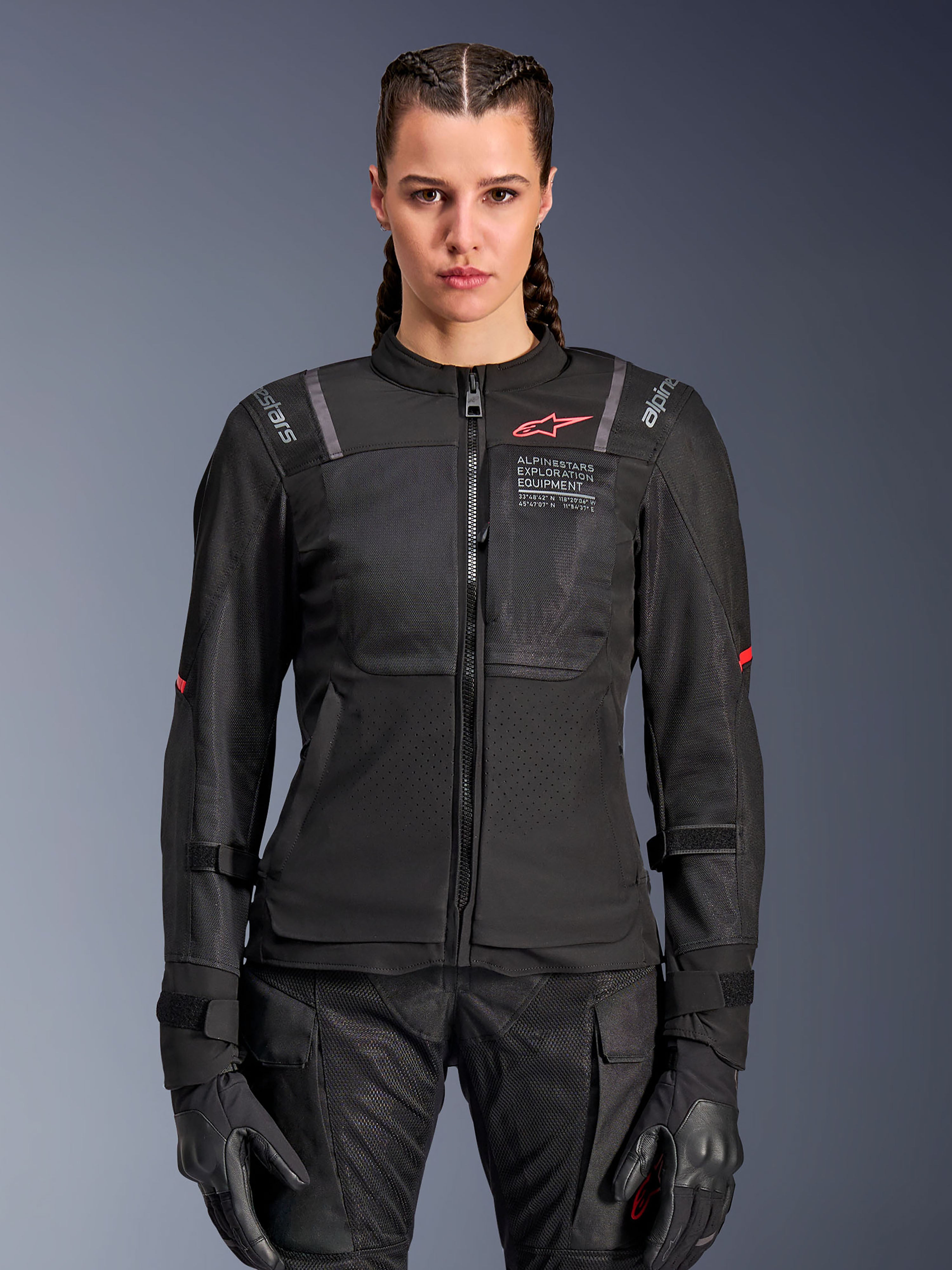 Veste Alpinestars Stella ST-2 Air pour femme, veste de moto pour femme, noire, vue de face sur modèle, avec panneaux en mesh, logo rouge sur la poitrine et marquage Alpinestars Exploration Equipment, portée avec des gants noirs et un pantalon de moto
