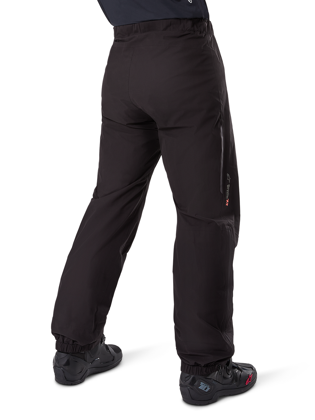 Doublure de pantalon Alpinestars Amt-8 Stretch Drystar® XF, noir, vue arrière montrant la doublure imperméable portée par-dessus des bottes de moto noires, avec marquage Drystar XF sur le bas de la jambe, chevilles élastiquées et matériau extensible léger pour l'adventure touring.