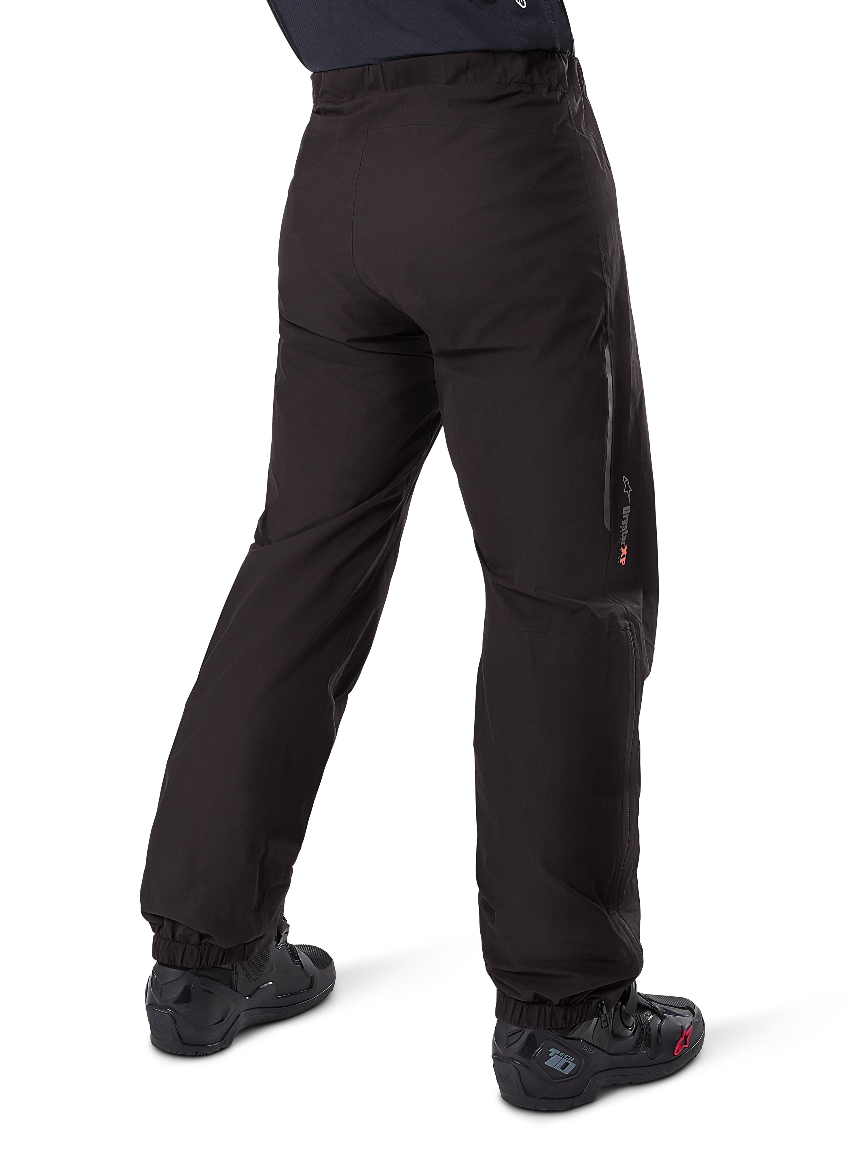 Doublure de pantalon Alpinestars Amt-8 Stretch Drystar® XF, noir, vue arrière montrant la doublure imperméable portée par-dessus des bottes de moto noires, avec marquage Drystar XF sur le bas de la jambe, chevilles élastiquées et matériau extensible léger pour l'adventure touring.