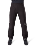 Doublure de pantalon Alpinestars AMT-8 Stretch Drystar® XF, noire, vue de face portée avec des bottes de moto noires, arborant le logo étoile gris et le marquage AMT sur la jambe, vêtement de moto polyvalent imperméable et coupe-vent