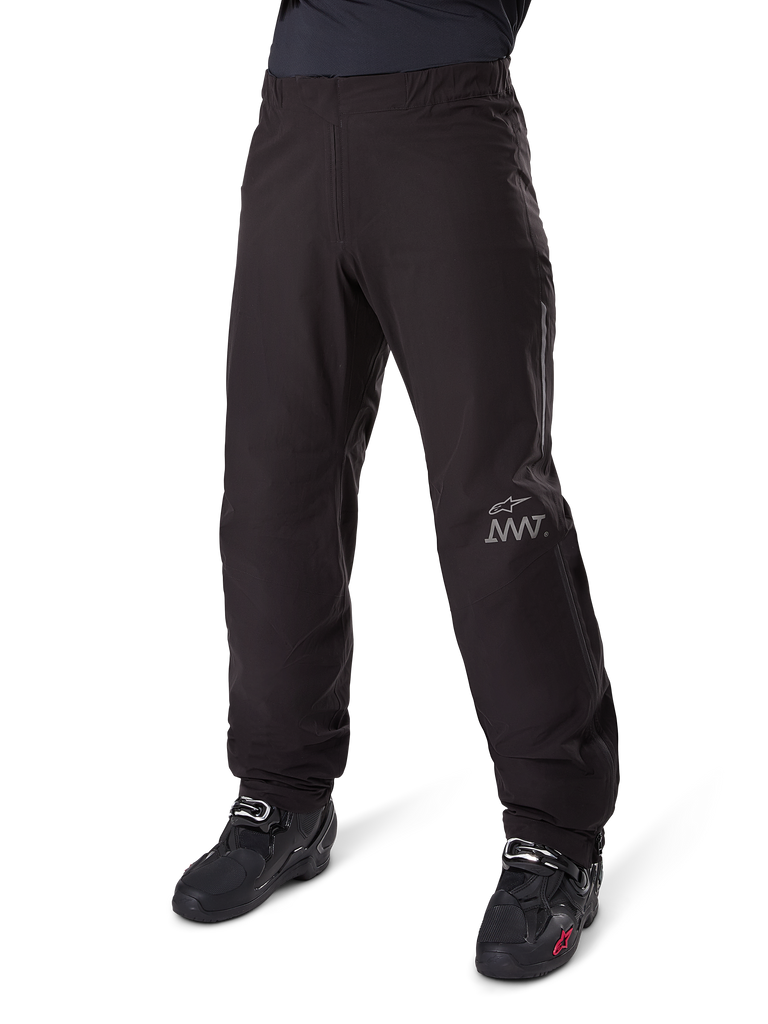 Doublure de pantalon Alpinestars Amt 8 Stretch Drystar® XF, pantalon de moto imperméable, noir, avec un logo AMT gris sur le bas de la jambe gauche, porté avec des bottes de moto noires, design fonctionnel pour l'aventure à moto par tous les temps