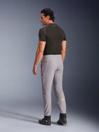 Alpinestars Aeroshell Hose, Mid Gray Yellow Fluo, Rückansicht eines männlichen Modells, das eine Stretch-Softshell-Motorradhose trägt, mit gelbem Astars-Logo auf der linken Wade, kombiniert mit einem schwarzen Base Layer und Motorradschuhen für eine moderne, sportliche Silhouette.