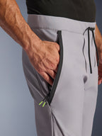 Alpinestars Aeroshell Hose, Mid Gray Yellow Fluo, Nahaufnahme der vorderen Reißverschlusstasche und des Bundes, schwarzer getapter Reißverschluss mit neongelben Enden, elastischer Bund mit schwarzem Kordelzug, Crossover-Sport-Softshell-Motorradhose