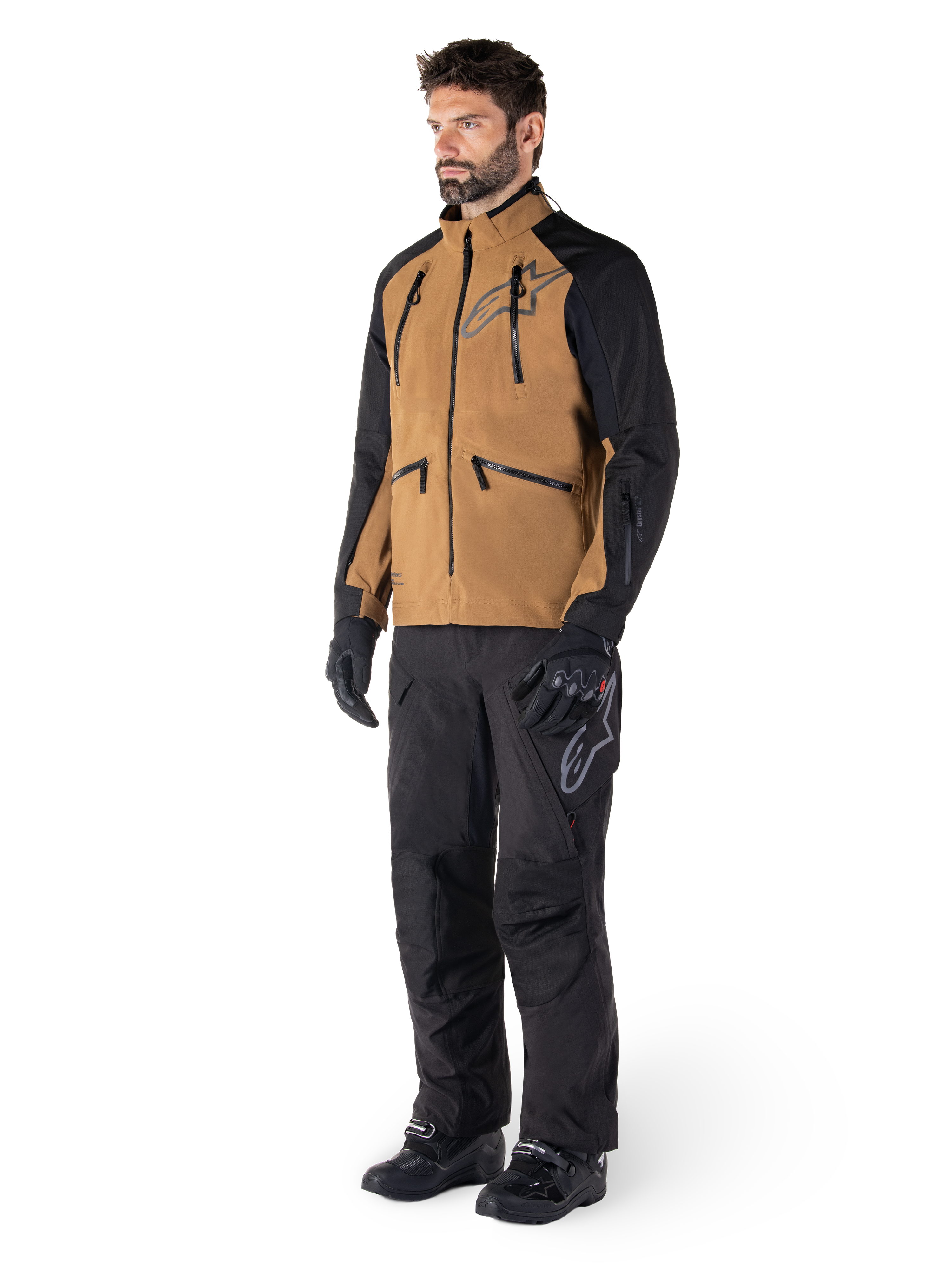 Alpinestars Hyde XT Drystar® Hose, Adventure-Motorradhose, Schwarz, getragen mit einer braun-schwarzen technischen Jacke, schwarzen Handschuhen und Stiefeln, mit einem Over-the-Boot-Design für Offroad- und Dual-Sport-Einsätze