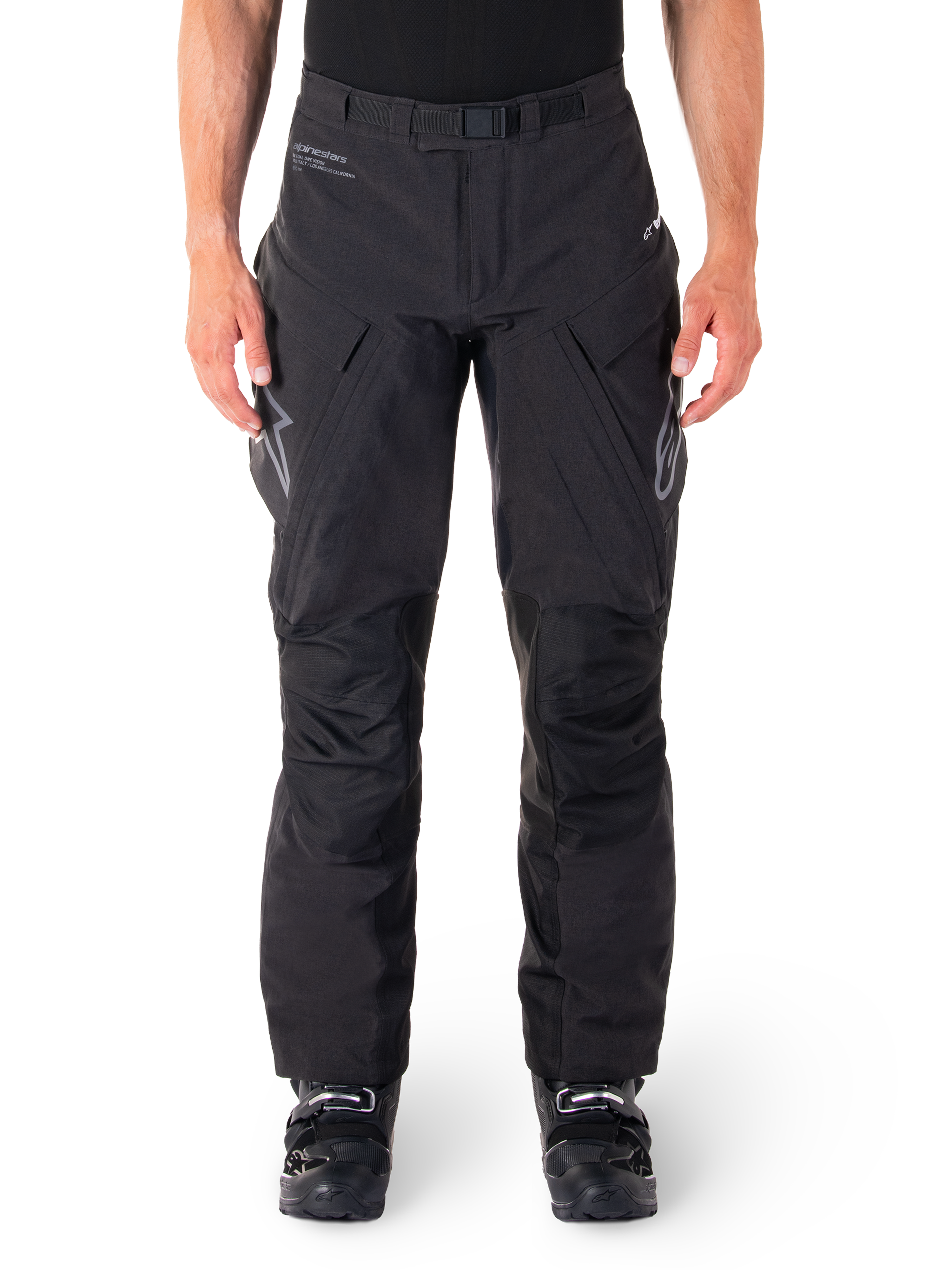 Alpinestars Hyde XT Drystar Hose, schwarze Adventure-Touring-Hose, getragen von einem Fahrer mit schwarzen Stiefeln, graue Logos auf den Oberschenkeln, integrierter Gürtel, verstärkte Kniepaneele, wasserdichte Textilkonstruktion.