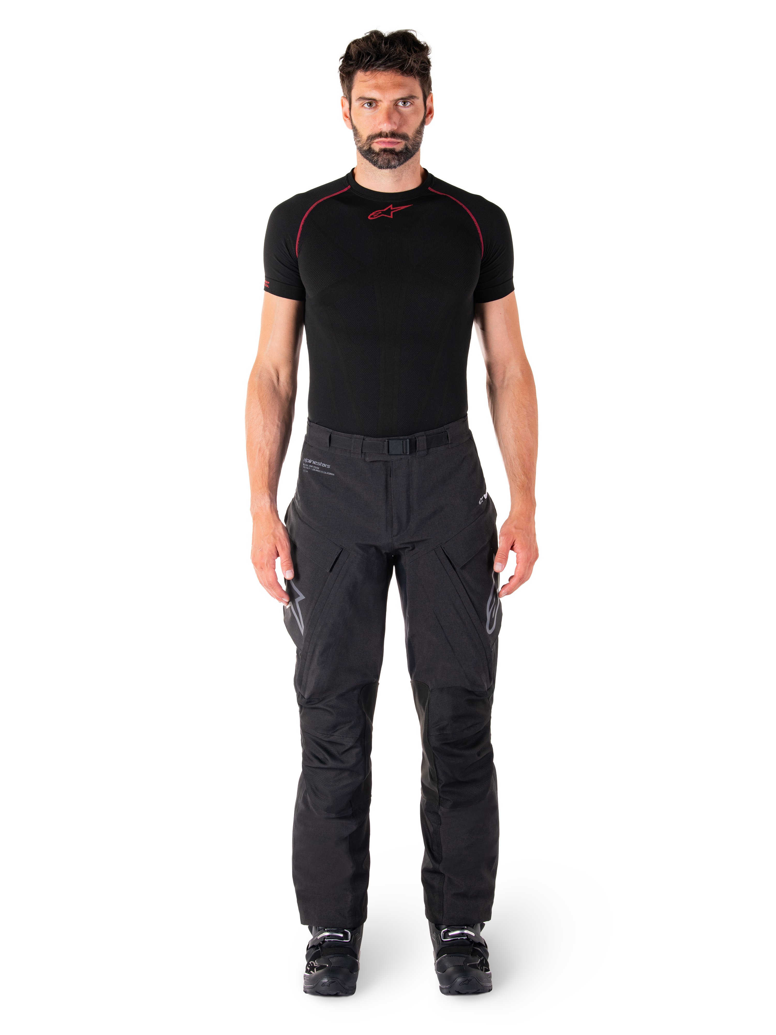 Alpinestars Hyde XT Drystar® Hose, Adventure-Touring-Motorradhose, Schwarz, getragen von einem Model mit schwarzem kurzärmeligem Base Layer und schwarzen Stiefeln, mit technischem Stretchmaterial, verstärkten Knieeinsätzen und ergonomischen Cargo-Taschen.