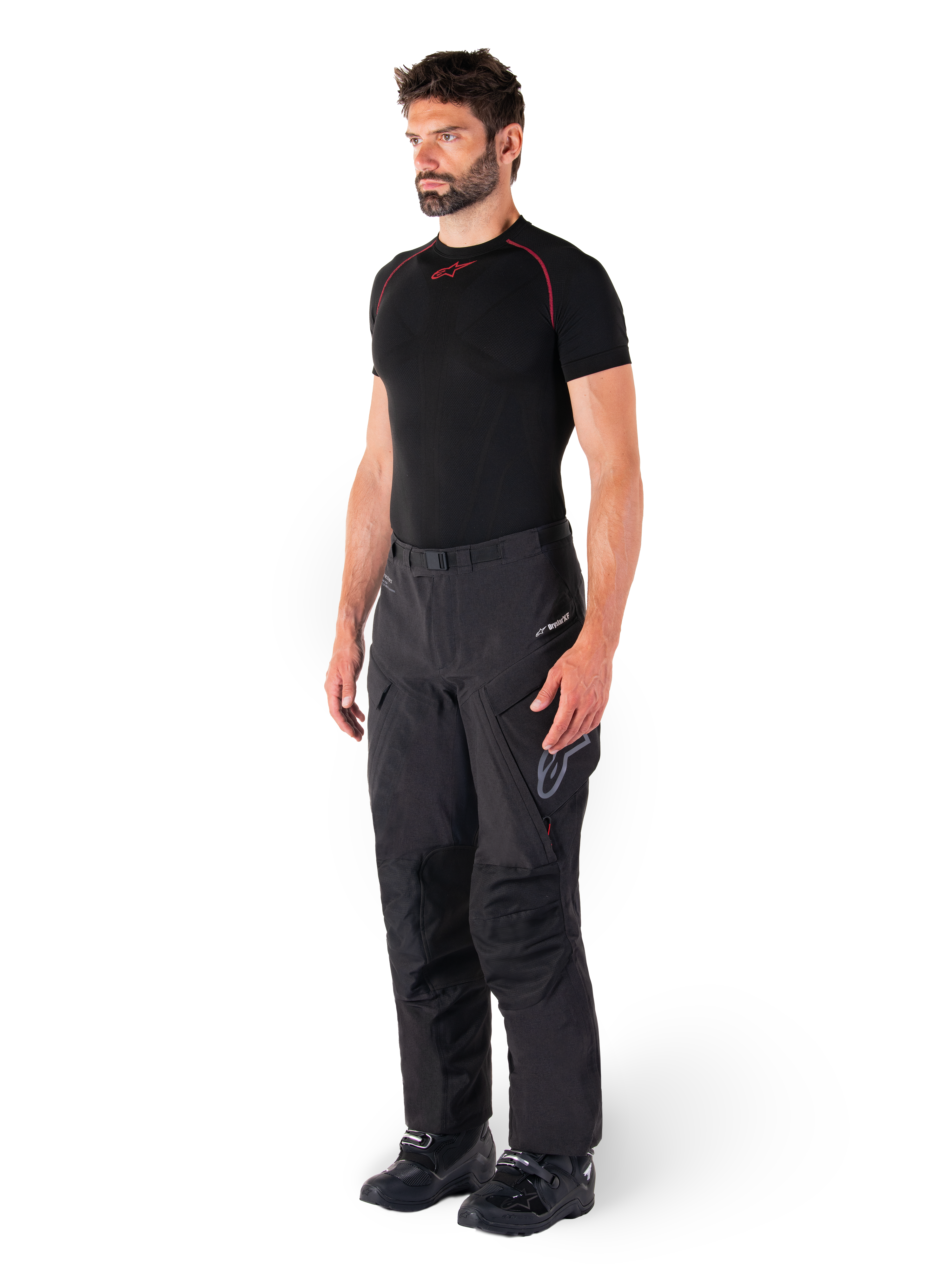 Alpinestars Hyde XT Drystar® Hose, schwarze Adventure-Touring-Motorradhose, getragen von einem Model mit einem schwarzen Kompressionsshirt und schwarzen Stiefeln, technische wasserdichte Konstruktion und Drystar®XF-Branding.