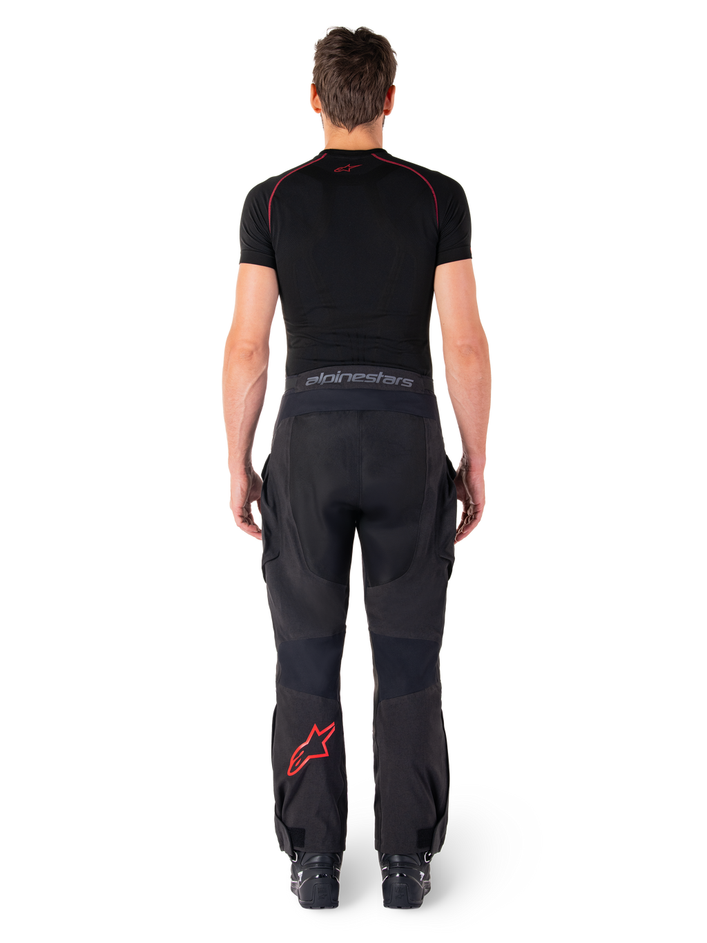 Alpinestars Hyde Xt Drystar® Hose, Adventure Touring Motorradhose, Schwarz und Bright Red, Rückansicht eines Fahrers, der die Hose und ein schwarzes Base Layer trägt, mit einem roten Stern-Logo auf dem linken Bein und grauem Branding am Hosenbund.