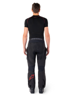 Alpinestars Hyde Xt Drystar® Hose, Adventure Touring Motorradhose, Schwarz und Bright Red, Rückansicht eines Fahrers, der die Hose und ein schwarzes Base Layer trägt, mit einem roten Stern-Logo auf dem linken Bein und grauem Branding am Hosenbund.