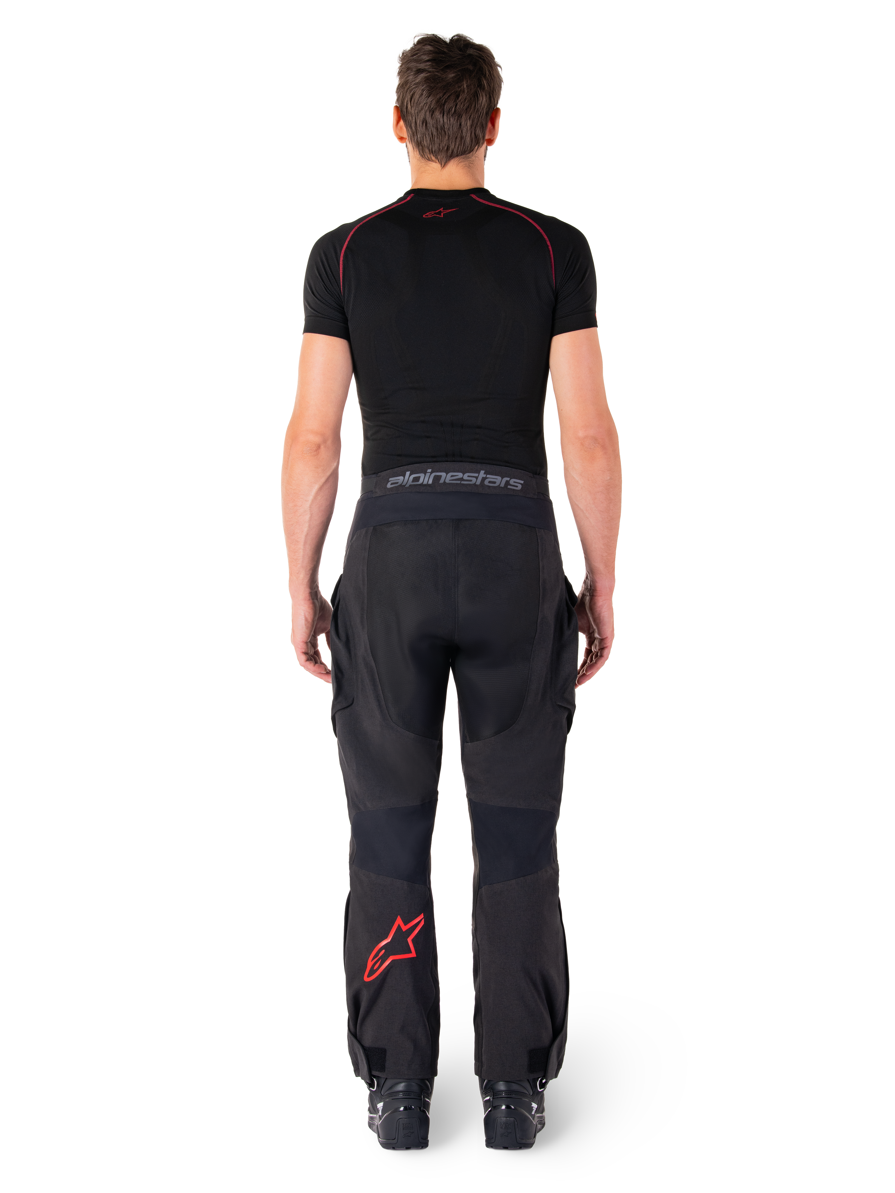 Alpinestars Hyde Xt Drystar® Hose, Adventure Touring Motorradhose, Schwarz und Bright Red, Rückansicht eines Fahrers, der die Hose und ein schwarzes Base Layer trägt, mit einem roten Stern-Logo auf dem linken Bein und grauem Branding am Hosenbund.