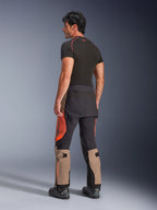 Alpinestars Halo Pro Drystar® XF gelamineerde broek in Walnut Rust Black, achteraanzicht van een mannelijk model met een adventure motorbroek met beige, oranje en zwarte panelen, gestyled met een zwarte basislaag en zwarte motorlaarzen, technische outdoor rijuitrusting