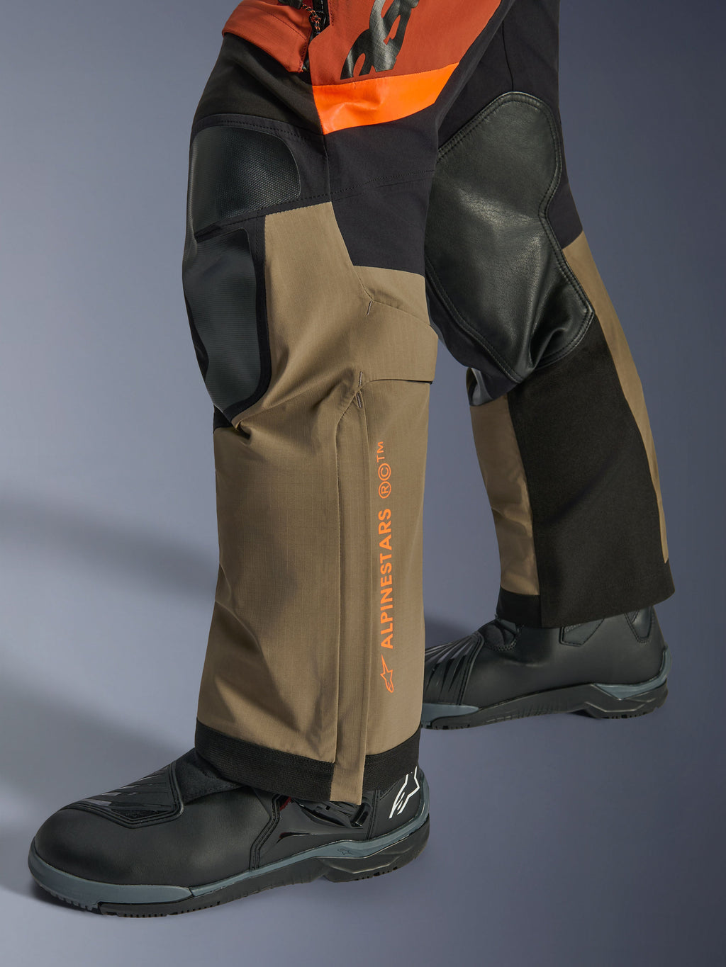 Alpinestars Halo Pro Drystar® XF Gelamineerde Broek, adventure motorbroek, Walnut Rust en zwart, detailopname met versterkte kniepanelen en oranje branding, gedragen met zwarte toerlaarzen, duurzame textielconstructie voor all-terrain rijden