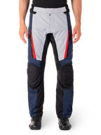 Alpinestars ST-1 Waterproof Pants, pantalon de moto touring, bleu foncé et gris clair avec des accents rouge vif, empiècements renforcés noirs aux genoux, vue de face porté avec des bottes noires, équipement de touring aventure imperméable