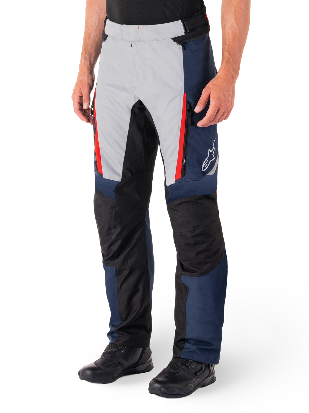Pantalon imperméable Alpinestars St-1, pantalon de moto touring, bleu foncé, noir et rouge vif, comprenant des panneaux avant gris clair avec des fermetures éclair rouges, des renforts noirs aux genoux et un logo Alpinestars blanc sur le côté, porté avec des bottes de moto noires.