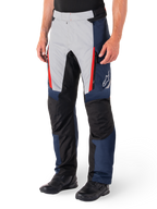 Pantalon imperméable Alpinestars St-1, pantalon de moto touring, bleu foncé, noir et rouge vif, comprenant des panneaux avant gris clair avec des fermetures éclair rouges, des renforts noirs aux genoux et un logo Alpinestars blanc sur le côté, porté avec des bottes de moto noires.