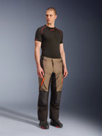 Pantalon Alpinestars Andes V4 Drystar®, pantalon de moto aventure touring, Walnut Black avec accents orange, porté par un mannequin avec un haut technique noir à manches courtes et des bottes noires, doté de panneaux textiles renforcés et de poches cargo, conception robuste pour rouler par tous les temps