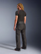 Pantalon Alpinestars Andes V4 Drystar® - Court, noir, vue de trois-quarts arrière sur un mannequin aux cheveux longs blonds, porté avec un haut technique noir à coutures rouges et des bottes de moto, design technique aventure touring avec panneaux textiles durables.