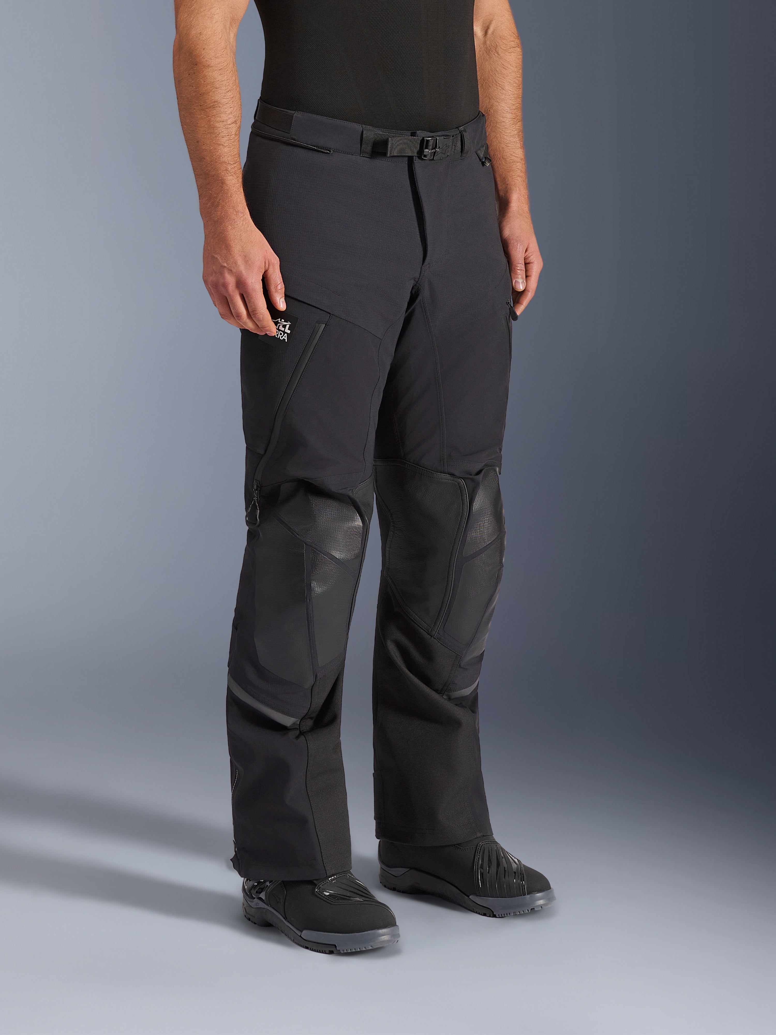 Alpinestars Andes Pro Drystar® XF Hose, Adventure-Touring-Motorradhose in Schwarz und Dunkelgrau, mit verstärkten Knieschutzzonen, Reißverschlusstaschen und verstellbarem Taillengurt, an einem Modell mit schwarzen Motorradstiefeln gezeigt.