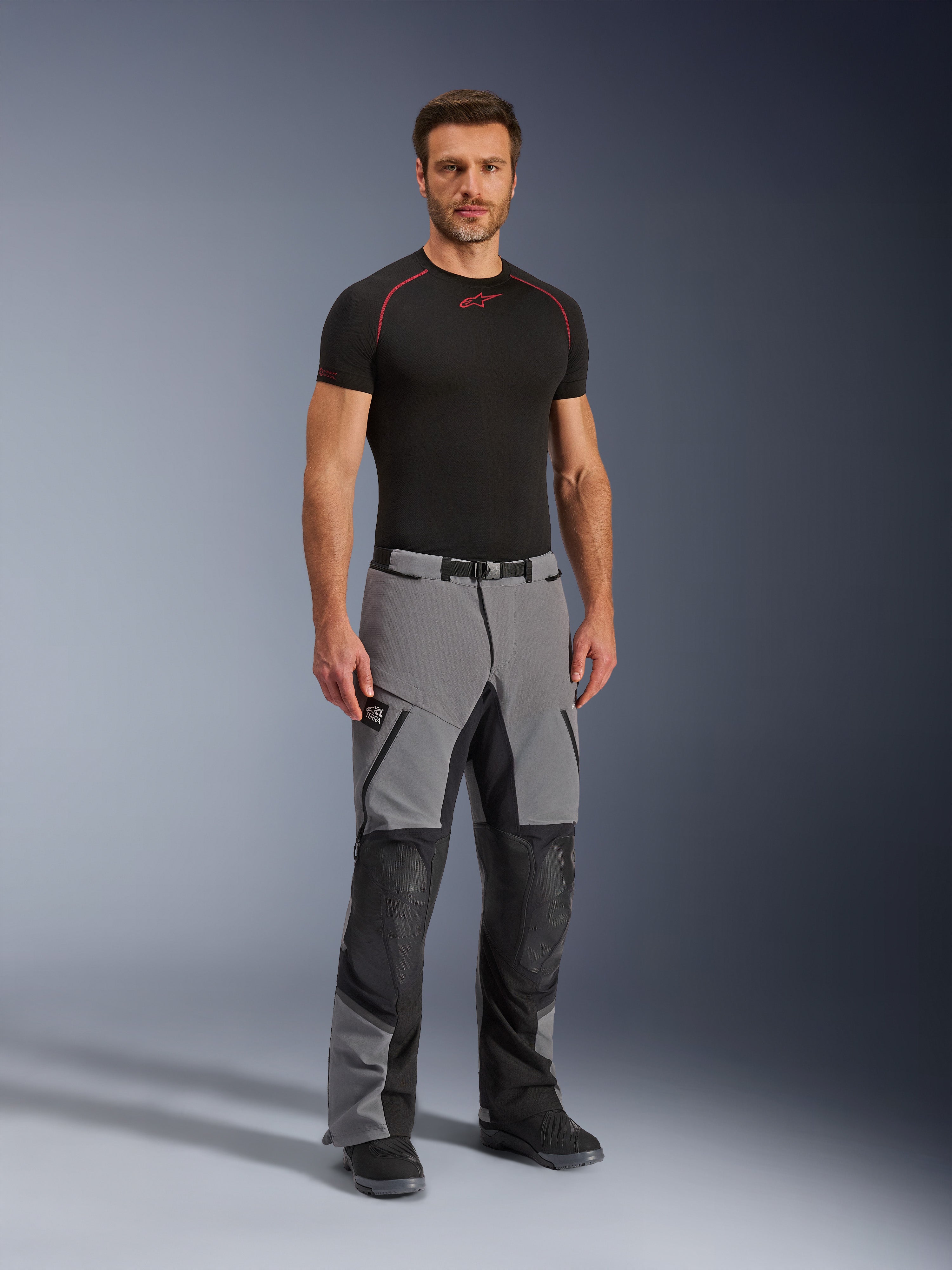 Alpinestars Andes Pro Drystar® XF Hose, Motorrad-Adventure-Hose, Dunkelgrau und Schwarz, getragen von einem Modell mit einem schwarzen technischen Base Layer, mit Multi-Panel-Konstruktion, wasserdichten Reißverschlüssen und verstärkten Zonen für Adventure-Fahrten.