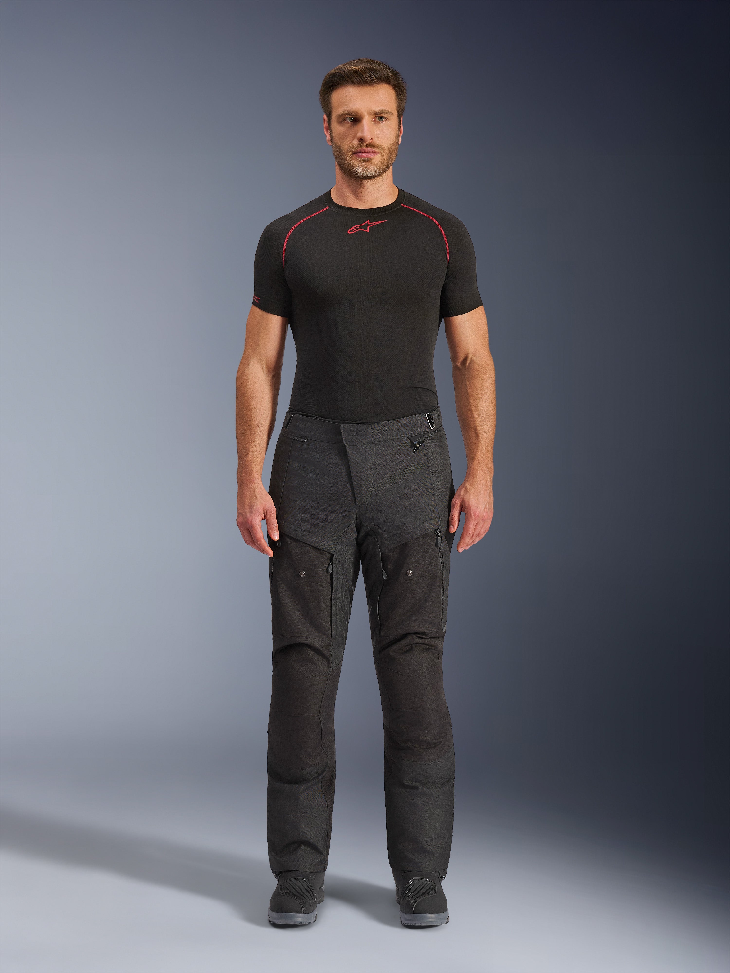 Alpinestars Cusco Drystar® broek, adventure motorbroek, zwart, volledig vooraanzicht op mannelijk model, voorzien van dijventilatie met rits en versterkte textielpanelen, gedragen met zwarte Alpinestars base layer