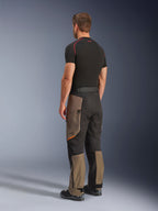 Pantalon Alpinestars Cusco Drystar®, pantalon de moto aventure, Walnut Black, vue de trois-quarts arrière porté avec une couche de base noire et des bottes, doté de panneaux textiles renforcés, de poches cargo zippées sur les cuisses et d'une coupe touring ergonomique.