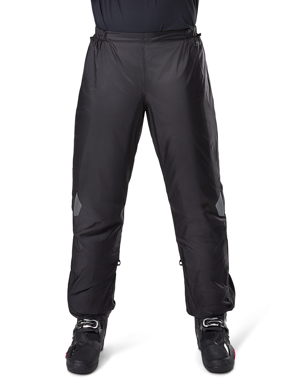 Pantalon Alpinestars Bogotá Pro Drystar 3 Saisons, pantalon de moto imperméable, noir, tissu technique léger avec empiècements réfléchissants aux genoux, porté en sur-pantalon avec des bottes de moto noires, conçu pour la protection contre les intempéries en touring d'aventure