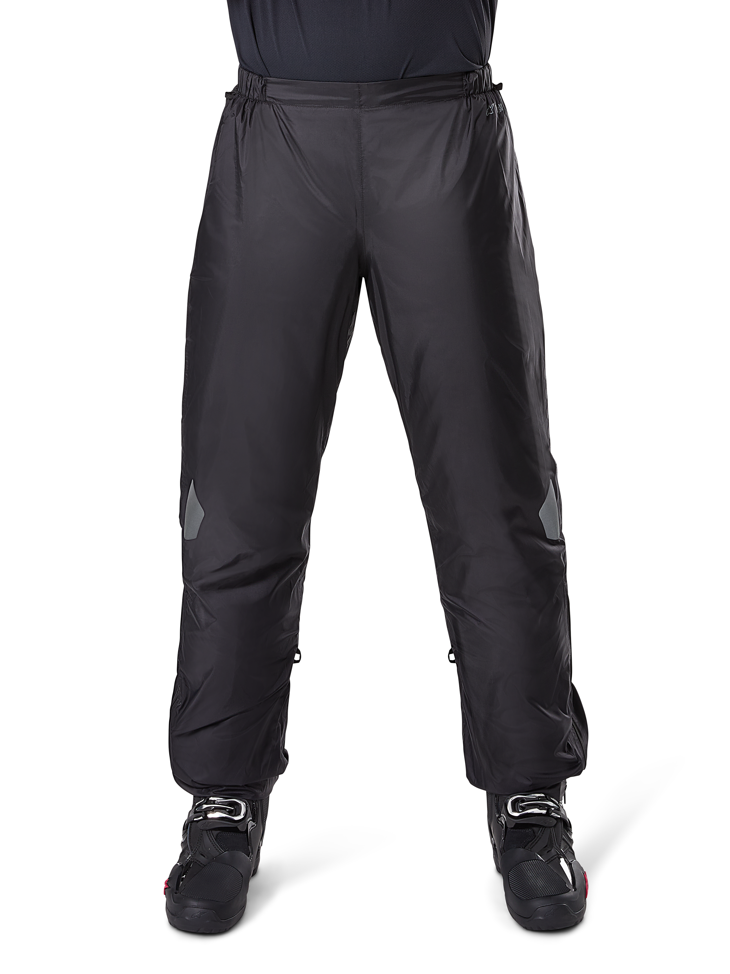 Pantalon Alpinestars Bogotá Pro Drystar 3 Saisons, pantalon de moto imperméable, noir, tissu technique léger avec empiècements réfléchissants aux genoux, porté en sur-pantalon avec des bottes de moto noires, conçu pour la protection contre les intempéries en touring d'aventure
