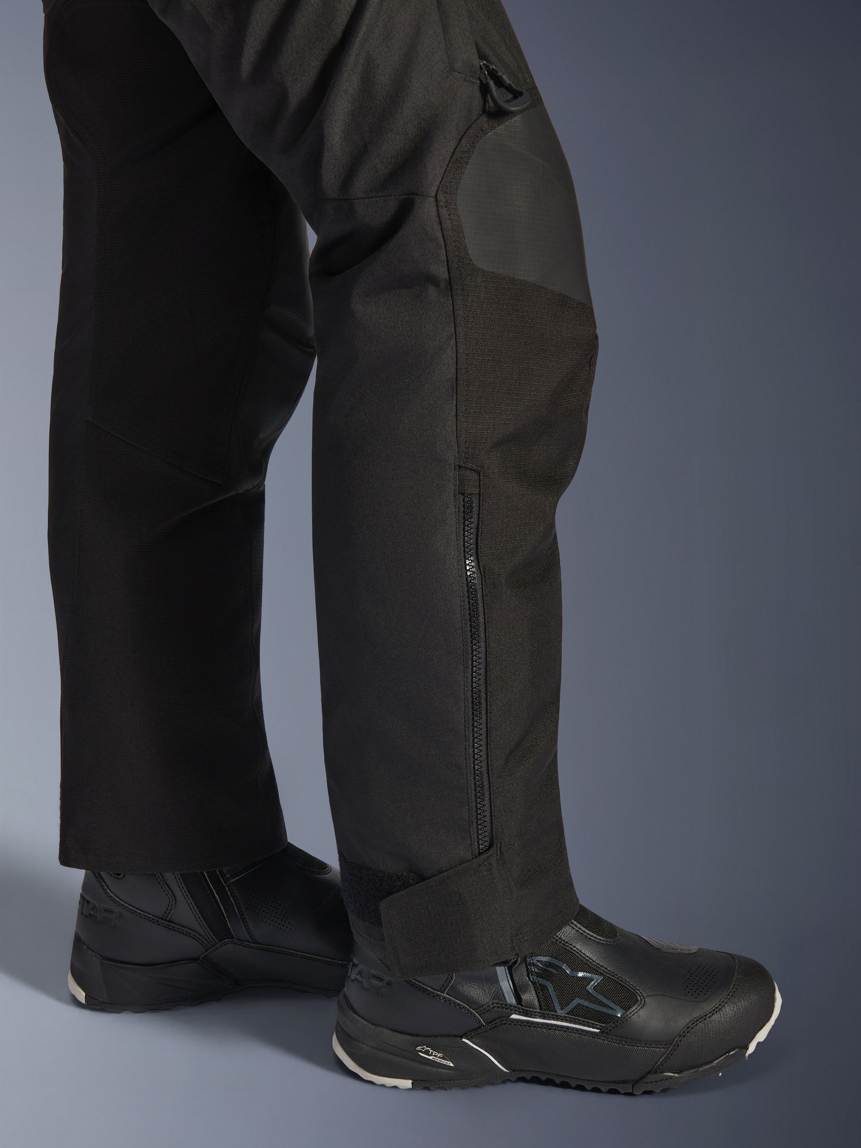 Pantalon Alpinestars Stella Andes V4 Drystar®, pantalon de moto pour femme, noir, gros plan sur le bas de la jambe avec fermeture éclair latérale et revers de cheville réglable, porté avec des bottes de moto Alpinestars noires