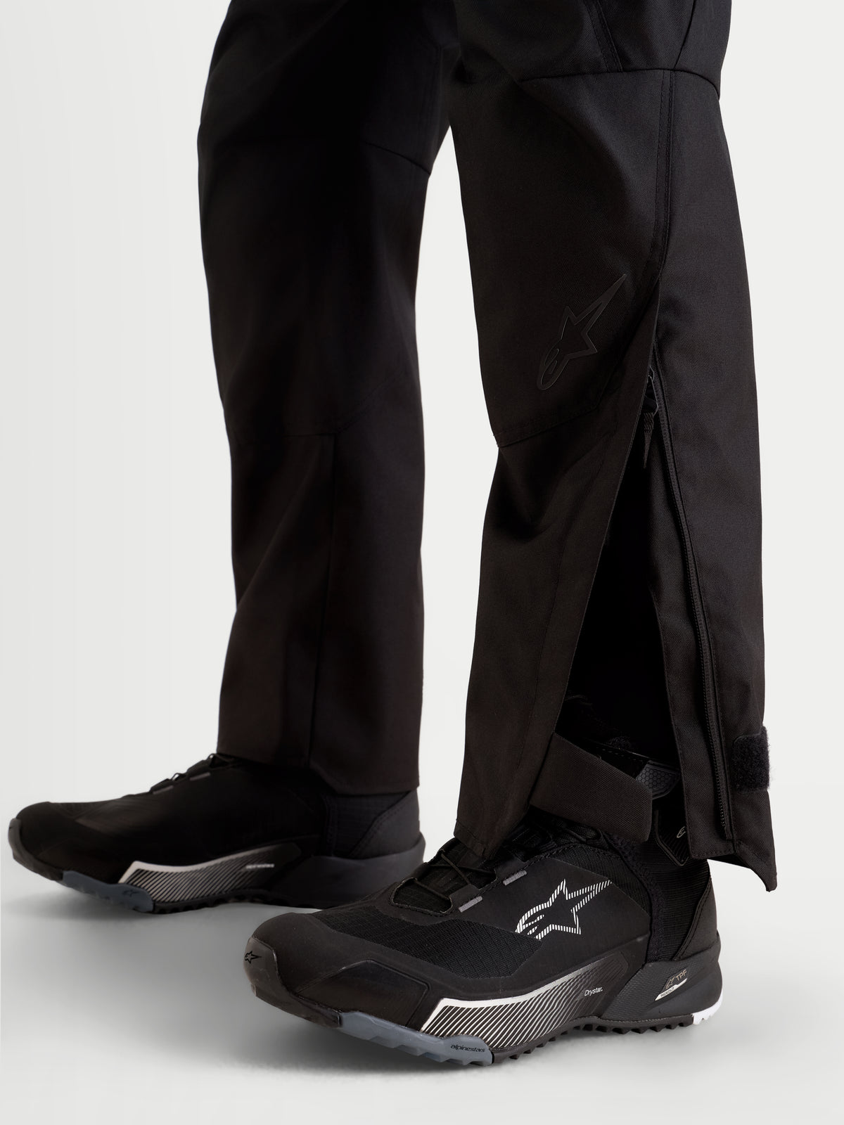 Alpinestars Stella C-1 Waterproof broek, zwarte motorbroek voor dames voor stedelijk gebruik, detailweergave van verlengde onderbeenopeningen met ritssluiting gedragen over motorlaarzen