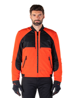 Parka imperméable Mootant Alpinestars en Spicy Orange et noir, veste de moto modulaire présentée dans une configuration de style bomber sur un mannequin homme, avec des empiècements en maille noire sur le haut de la poitrine, le buste et les manches orange vif, une fermeture éclair frontale et un col côtelé, portée avec des gants et un pantalon noirs.