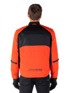 Parka imperméable Alpinestars Mootant, veste de moto, orange épicé et noir, vue arrière, avec le haut du dos en maille noire et un panneau inférieur orange arborant le logo MO.ST.EQ., portée avec un pantalon et des gants noirs.