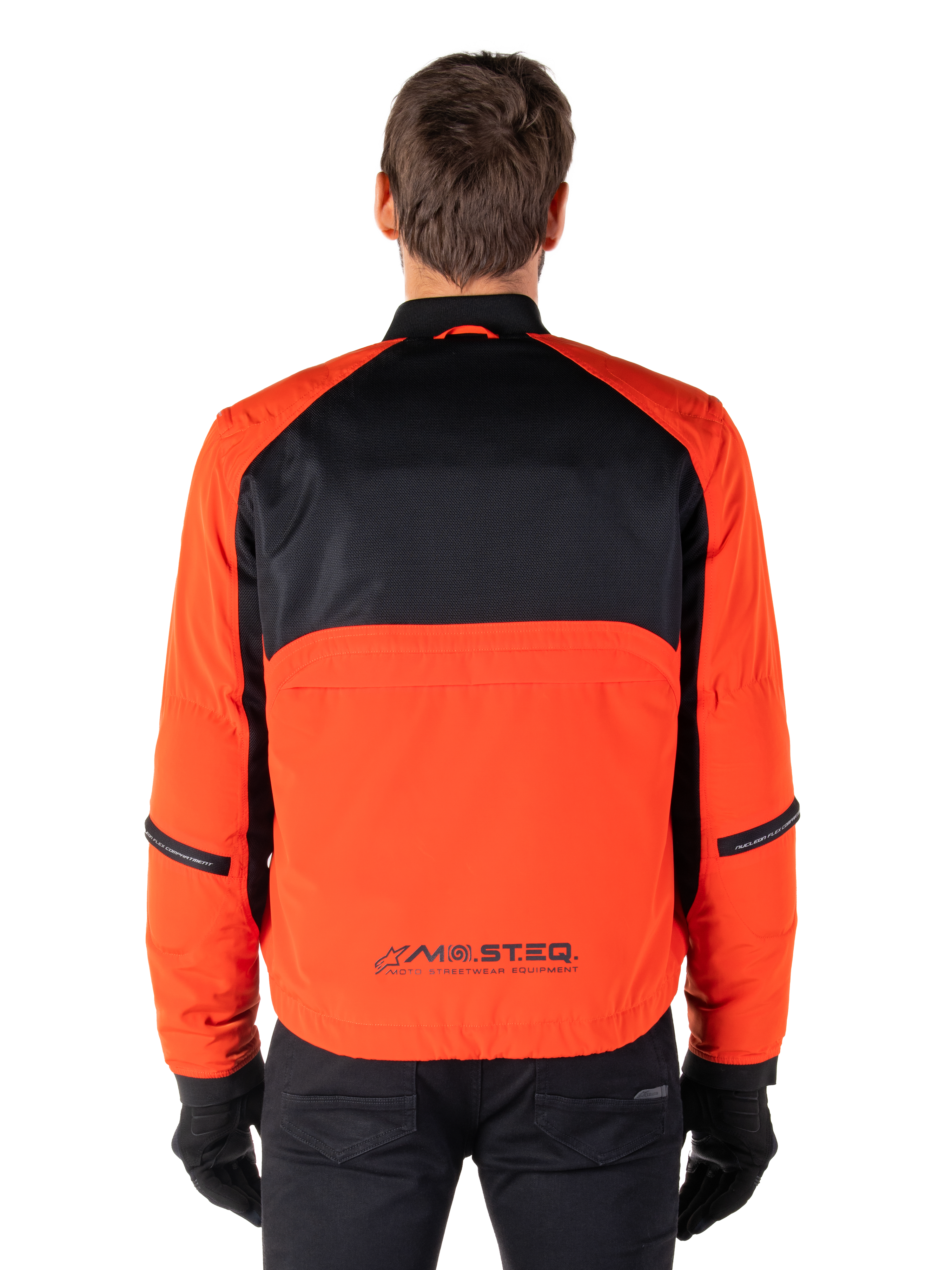 Parka imperméable Alpinestars Mootant, veste de moto, orange épicé et noir, vue arrière, avec le haut du dos en maille noire et un panneau inférieur orange arborant le logo MO.ST.EQ., portée avec un pantalon et des gants noirs.
